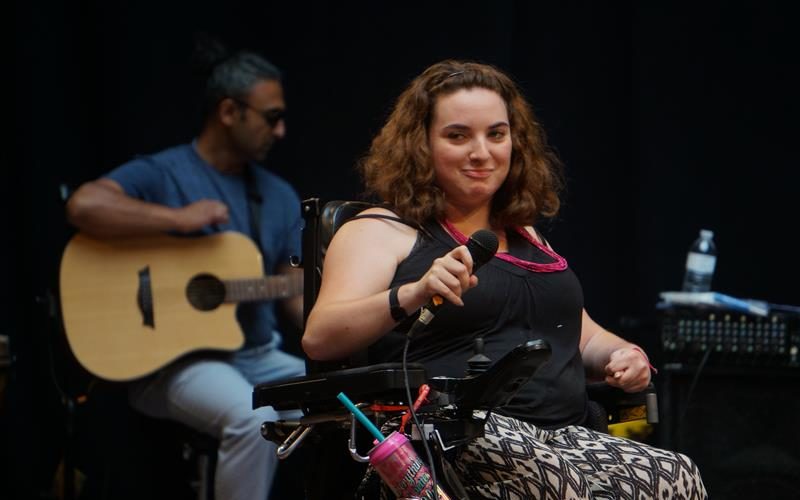 Jessica singing on stage with a microphone, with a person playing the guitar in the background