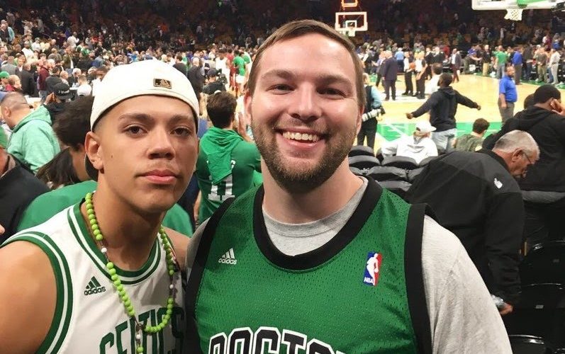 Matt and his mentee pose together in front of the basketball court at the TD Garden, both wearing Celtics gear.