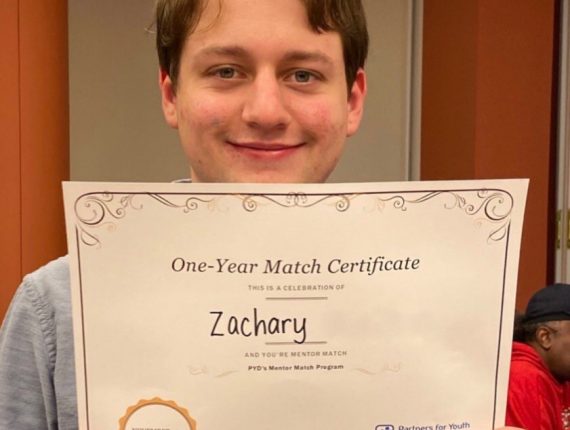 Zachary, a PYD youth smiles for a photo as he holds up his one year match certificate