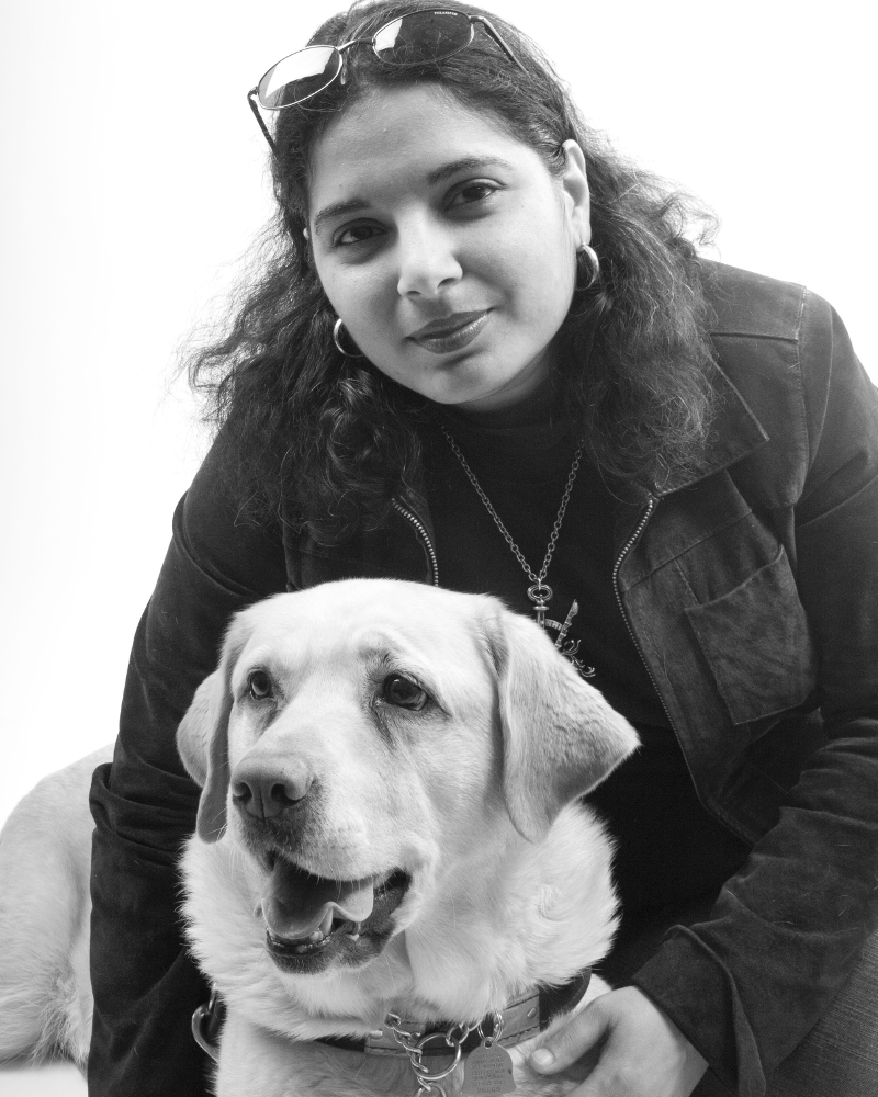 Day, an Arab-American woman with dark hair and suede jacket sitting with Veni, yellow lab guide dog
