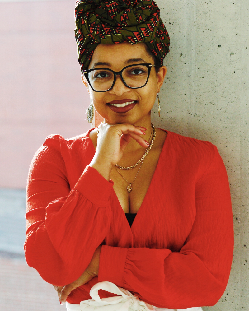 Headshot of Keri Gray. She is a Black woman wearing an orange shirt with a green and orange headwrap. She is also wearing glasses.