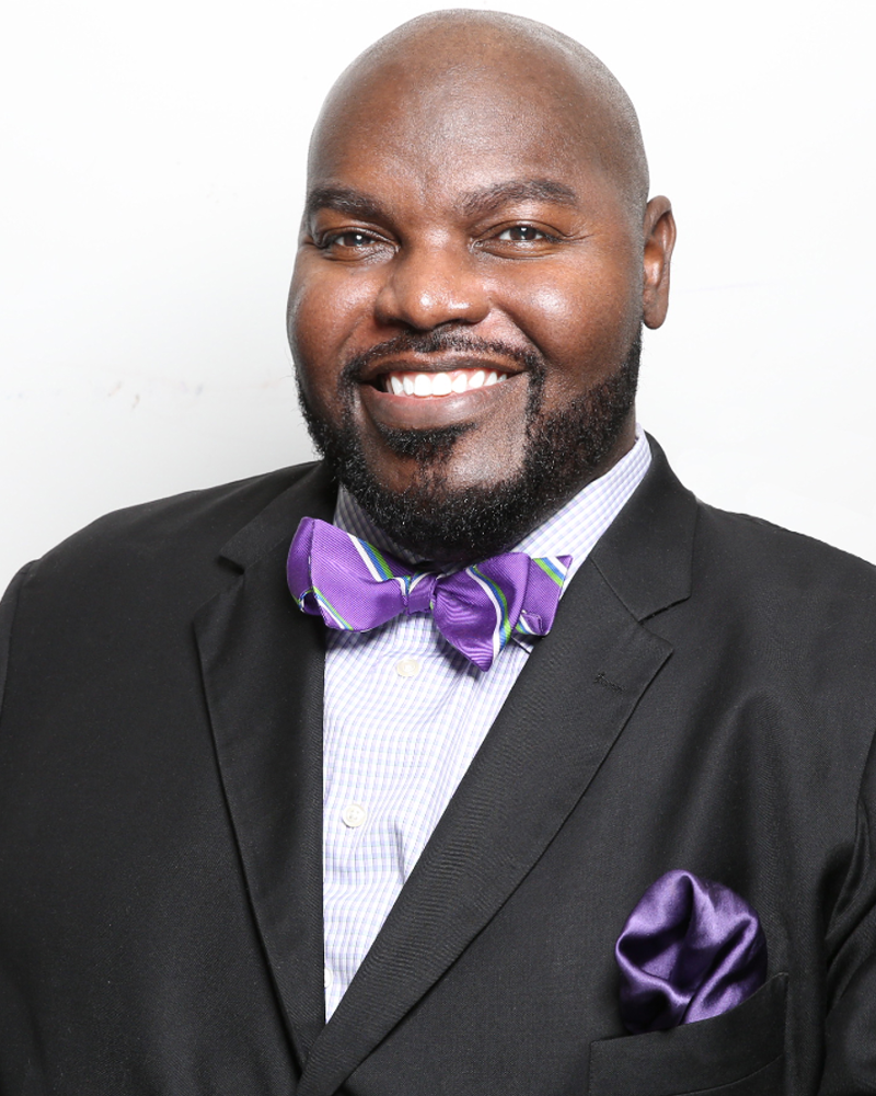 Dr. LaMondre Pough. Smiling bald black man wearing a dark suit and purple bow tie.
