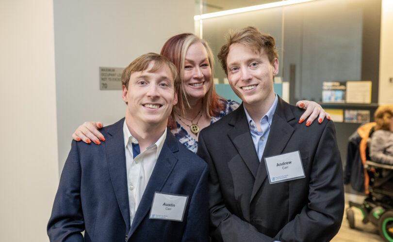 Woman in blue patterned dress with her arms around two men in navy suits