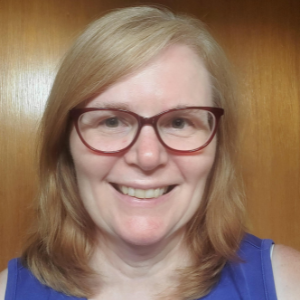 Woman with blonde hair wearing blue shirt and brown glasses