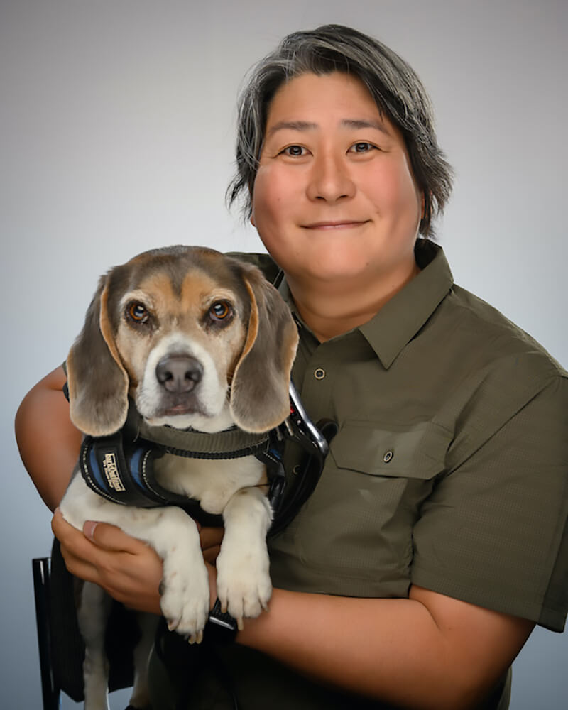 A photo of Karen who has short hair, is wearing a green shirt and is holding her dog.