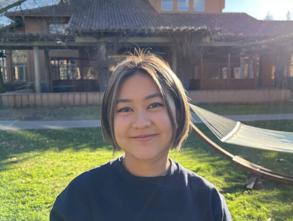 Arisa has bob-length hair with highlights, and is smiling in front of a building while wearing a Stanford sweatshirt.