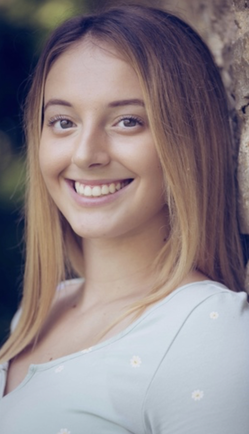 Skyler has medium blonde long hair and is smiling at the camera while wearing a light blue shirt.