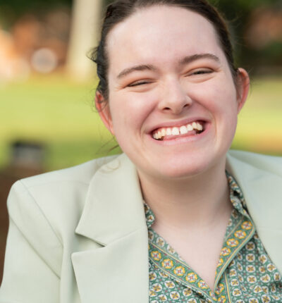 Lillian is smiling while wearing a light green blazer with a patterned green shirt underneath.