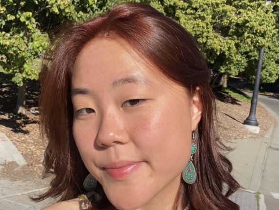 Nico has shoulder length reddish hair, and is wearing turquoise earrings and a pearl necklace.
