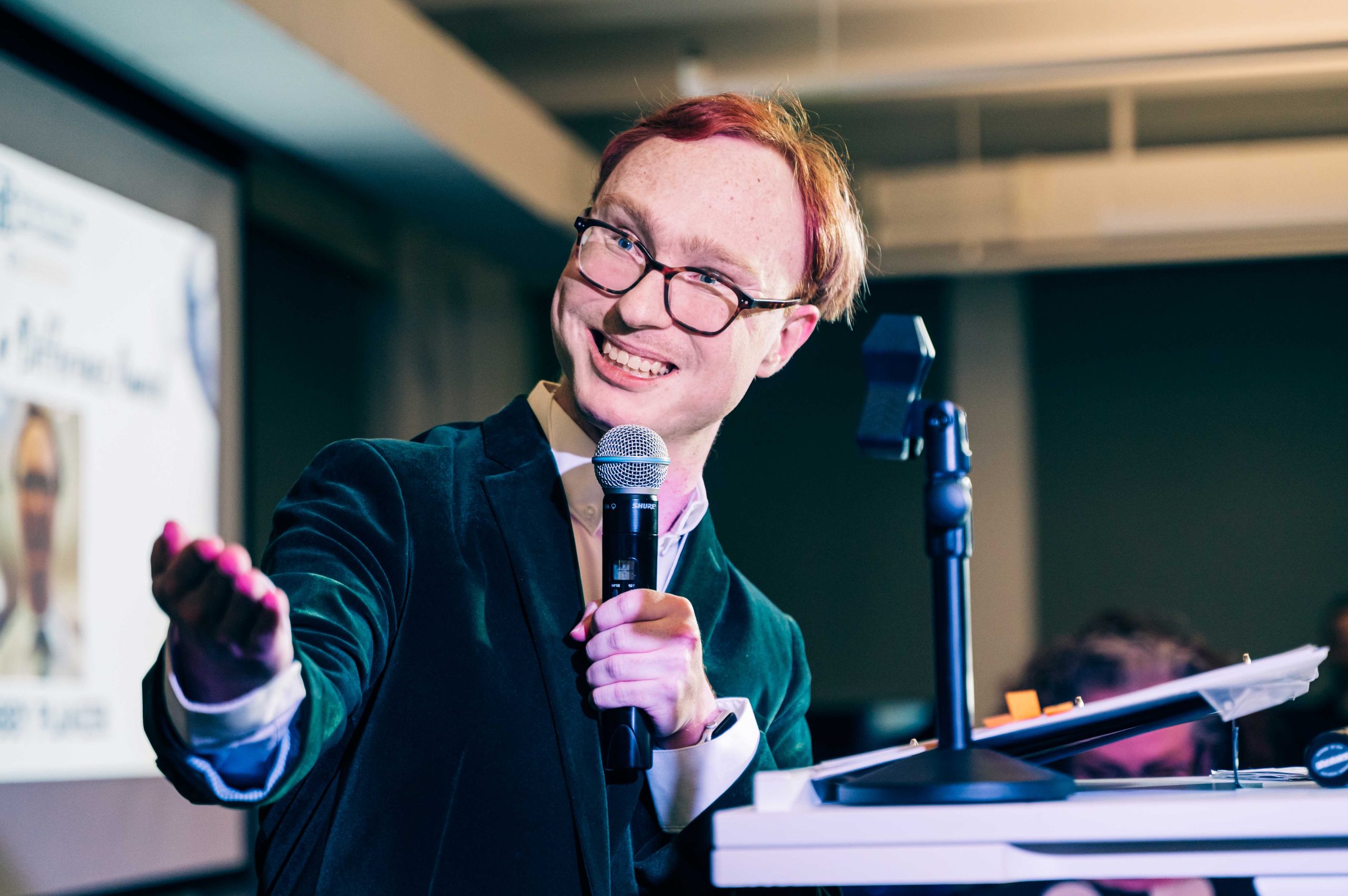 Honoree, Bobby Planzer is holding a microphone and gesturing out with his right hand, smiling