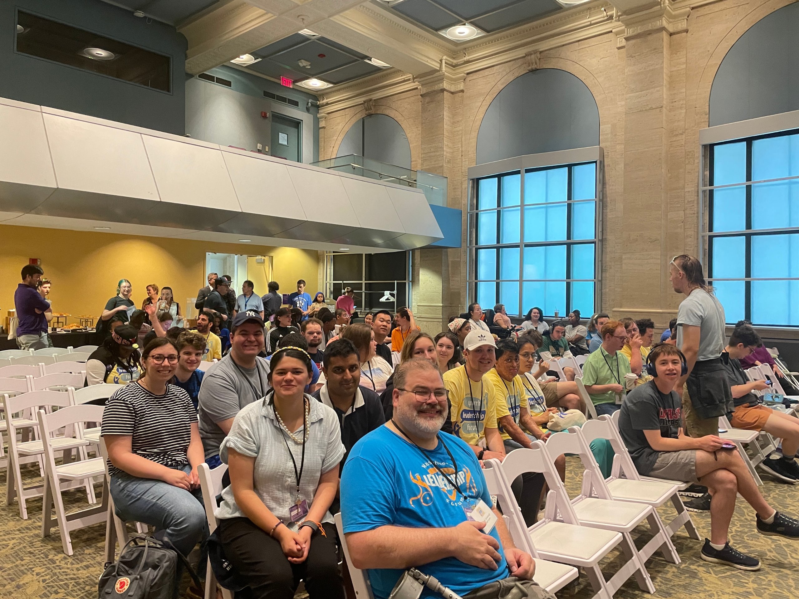 Participants sit in a large hall, smiling at the camera.